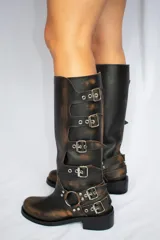 Botas de cuero marrón con efecto gastado, caña alta y hebillas metálicas.