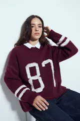 Sweater de tejido de punto color blanco con estampado numérico '87' en negro en el frente y detalles de rayas horizontales en las mangas. Presenta cuello redondo y un calce relajado.