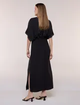 Vestido largo amarillo de corte fluido con escote en V, mangas cortas amplias y apliques de tachas en el escote y puños. Posee cintura elastizada fruncida y falda larga con tajos laterales en el ruedo.