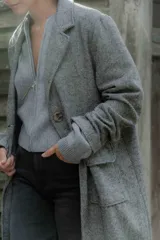 Tapado de corte recto y largo midi, confeccionado en tejido con textura de espiga en tonos grises. Presenta solapas clásicas, cierre frontal con botones y bolsillos laterales amplios con solapa.