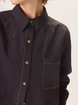 Camisa de manga larga con diseño combinado. Presenta mangas y parte superior delantera y trasera en color negro liso, mientras que el panel central de la espalda destaca por un estampado animal print de leopardo. Cuenta con cuello clásico, cierre frontal de botones y puños abotonados.