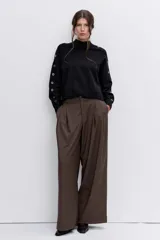 Sweater de punto negro con cuello alto y detalle de ojalillos metálicos a lo largo de las mangas. Presenta un corte holgado con puños y ruedo acanalados.