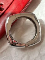 Brazalete rígido de diseño cuadrado con acabado metálico brillante en tono dorado.