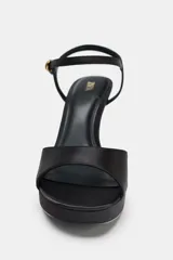 Sandalia de tacón fino alto y plataforma, confeccionada en tela satinada color negro. Cuenta con una tira delantera y cierre mediante tira con hebilla en el tobillo.