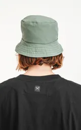 Gorro tipo bucket de color verde militar, con ala ancha y un pequeño parche negro con un logo blanco en el frente.