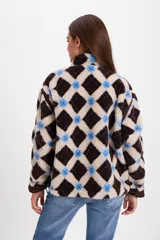 Campera de corderito sintético con diseño a cuadros en tonos marrones y negros. Presenta cuello alto, cierre frontal completo y detalles de paneles en color marrón liso. El diseño es de silueta holgada, largo tipo crop y cuenta con un cordón elástico ajustable en el ruedo.