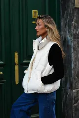 Chaleco puffer beige, sin mangas, con cuello alto, cierre frontal de cremallera y bolsillos laterales.
