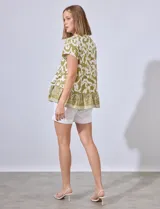 Blusa de lino con cuello a la base, escote en V y abertura central con botones. Presenta un corte en la cintura con frunces y terminación en el ruedo con volados.