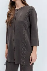 Cardigan negro de punto con acabado brillante, cuello redondo, cierre frontal de botones y detalle de cordones laterales entrelazados. Presenta mangas tres cuartos con diseño acampanado.