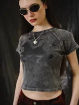 Remera baby tee de algodón gris con efecto stone wash, calce ajustado al cuerpo y largo corto, con mangas cortas y cuello redondo. Cuenta con un gran estampado en serigrafía de un animal mitológico en la parte frontal.