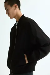 Campera bomber liviana color negro, con cuello, puños y dobladillo acanalados, cierre frontal metálico y bolsillos laterales ribeteados.