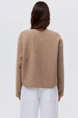 Chaqueta de sherpa suave con cuello redondo, corte holgado y cierre frontal con botones metálicos. Presenta ribetes de cinta en los bordes.