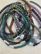 Collar artesanal compuesto por cuentas de piedra volcánica en diversos tonos y tamaños, con una perla natural de río como dije central y cierre metálico dorado.