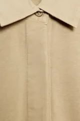 Polo oversize de algodón color beige, de manga larga, con cuello camisero y cierre frontal de botones ocultos.