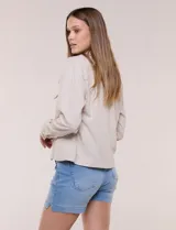Camperita liviana de silueta recta y calce relajado de lino color beige, con cuello camisero, cartera frontal con botones símil madera y bolsillos aplicados con solapa en el pecho. Presenta mangas largas con puños de cierre abotonado y costuras reforzadas a tono.