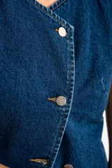 Chaleco de denim azul con cierre cruzado con botones metálicos.