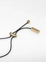 Collar largo con cordón negro regulable y dije metálico rectangular de diseño abstracto con efecto arrugado. El dije combina acabados en tonos dorado y plateado, y cuenta con terminales metálicos en el cierre.