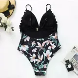 Malla enteriza bicolor de diseño combinado, con parte superior lisa en color negro de escote en V pronunciado con bordes ondulados, y parte inferior con estampado botánico de hojas verdes y flores rosadas sobre fondo negro. Cuenta con tirantes finos regulables.