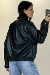 Chaqueta de ecocuero color marrón, de corte oversize, con cuello clásico, cierre frontal metálico, bolsillos laterales con solapa y puños con broches a presión.