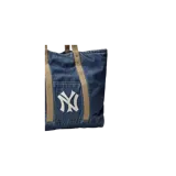 Cartera tipo shopper de denim azul, con asas y detalles en color tostado. Presenta un bolsillo frontal con el logo bordado de los New York Yankees en color blanco.