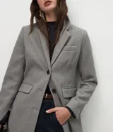 Abrigo largo de corte slim, color gris con textura jaspeada. Presenta solapas clásicas, cierre frontal con botones, bolsillos laterales con solapa y abertura trasera. Incluye forro interno.