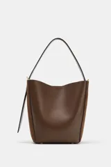 Bolso tipo saca con diseño estructurado, confeccionado en una combinación de cuero liso y gamuza en tono marrón. Cuenta con asa de hombro fija, cierre imantado y detalles metálicos en dorado.