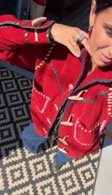 Chaqueta roja de cuero 100% artesanal, con pasamanería y detalles de costura en tiento. Posee bolsillos plaqué frontales, cuello camisero, botones de cuero alargados tipo duffel y forro interno.
