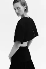 Cropped top negro con leve brillo, de manga corta, escote redondo, hombros caídos y cierre visible en la espalda.