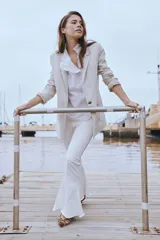 Blazer de lino color beige, con solapa y puños con detalles sutiles de volados, cierre frontal de un botón y bolsillos ojal.