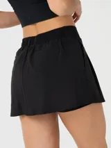 Falda deportiva tipo skort color negro, con diseño de tablas, trabillas para cinturón y bolsillos laterales. Incluye short interior con bolsillo integrado, confeccionada en tejido con tecnología Aircool de secado rápido.