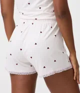 Short de pijama de poliéster color rosado con estampado de pequeños corazones oscuros, cintura elastizada con botones frontales decorativos y terminación de encaje en los bajos.