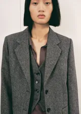 Blazer de corte recto confeccionado en tejido de mezcla de lana jaspeada. Presenta cuello con solapas de muesca, cierre frontal con botones, mangas largas con puños abotonados, dos bolsillos de parche frontales y abertura posterior en el bajo. Incluye forro interior.