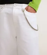 Bermuda ancha tipo baggy de sarga de algodón, color blanco, con cierre tradicional, bolsillos y detalle de cadena metálica colgante.