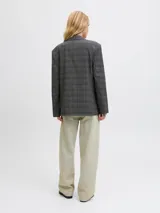 Blazer de sarga con diseño oversize, cuello con solapas y cierre frontal de dos botones. Presenta un estampado de cuadros en tonos gris oscuro y una estructura definida.
