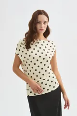 Top de poliéster negro con estampado de lunares blancos, diseño al cuerpo y cuello asimétrico de manga corta.
