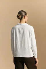 Blusa de algodón color azul con textura bordada, cuello con volado y cierre frontal con botones. Presenta mangas largas y un calce relajado.