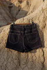 Short de denim elastizado en color azul marino, con tiro alto y lazo ajustable en la cintura. Presenta pespuntes en contraste, bolsillos frontales y cierre frontal con botón y cremallera.