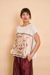 Blusa blanca de corte holgado, con mangas cortas y un panel frontal de seda con estampado botánico y floral en tonos rosados, bordó y verdes.