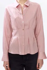 Camisa entallada de mezcla de viscosa en color rosado, con efecto arrugado y bajo levemente acampanado. Presenta cuello camisero, cierre frontal de botones, canesú en la espalda y pliegues en la cintura que definen la silueta. Cuenta con mangas largas y puños abotonados.