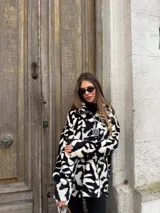 Buzo de peluche con estampado animal print en blanco y negro, de corte holgado, cuello alto y cierre frontal parcial con tirador metálico.