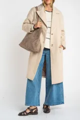 Tapado largo de corte oversize en color beige, con solapas clásicas y cierre frontal con botones. Presenta un diseño minimalista y elegante, ideal para un look sofisticado.