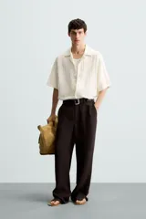 Camisa de calce relajado confeccionada en tejido de algodón color beige. Presenta un diseño de jacquard con líneas verticales desflecadas, cuello tipo bowling, manga corta y cierre frontal con botones.