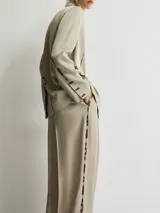 Blazer de corte recto confeccionado en viscosa, color gris topo. Presenta solapas clásicas, cierre frontal de dos botones y mangas largas con botones en los puños. Destaca por su diseño con detalles de efecto pintura en solapas, costuras y bolsillos. Incluye un bolsillo con solapa en el frente y abertura en la espalda.