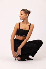 Top tipo corset negro con copas armadas y diseño drapeado en el busto. Presenta una base curva decorada con ojalillos metálicos y tachas plateadas. Incluye breteles intercambiables y cierre posterior con ganchos regulables.