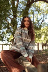 Campera de jean con cierre frontal y cuello tipo bomber, presenta un estampado horizontal con motivos paisajísticos y geométricos en tonos azules, marrones y beige. Posee puños de tela elástica en color blanco.