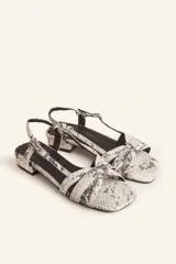 Sandalias bajas con estampado de piel de serpiente en tonos blanco y negro. Tiras finas entrecruzadas en el empeine, pulsera al tobillo con hebilla ajustable y pequeño tacón cuadrado.