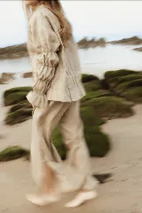 Camisa de lino color marrón rojizo, con cuello clásico y botones frontales blancos. Presenta pliegues verticales en el torso y mangas largas abullonadas con frunces elásticos en los puños.