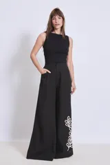 Pantalón negro de corte palazzo con bolsillos laterales y apliques bordados de hojas en color crudo en una pierna.