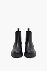 Bota tipo chelsea de caña media, con diseño combinado en cuero liso negro en la parte frontal y gamuza negra en el talón, con detalle de panel trasero en cuero marrón oscuro. Cuenta con elásticos laterales y suela track de goma negra.