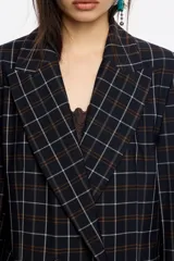 Chaqueta de corte sastre cruzada con diseño de cuadros, cuello con solapa, botones frontales y bolsillos con solapa. Presenta un largo medio y mangas largas rectas.